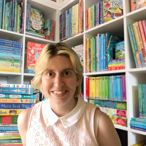 Me, a white woman smiling in front of a bookshelf filled with a rainbow of colorful spines